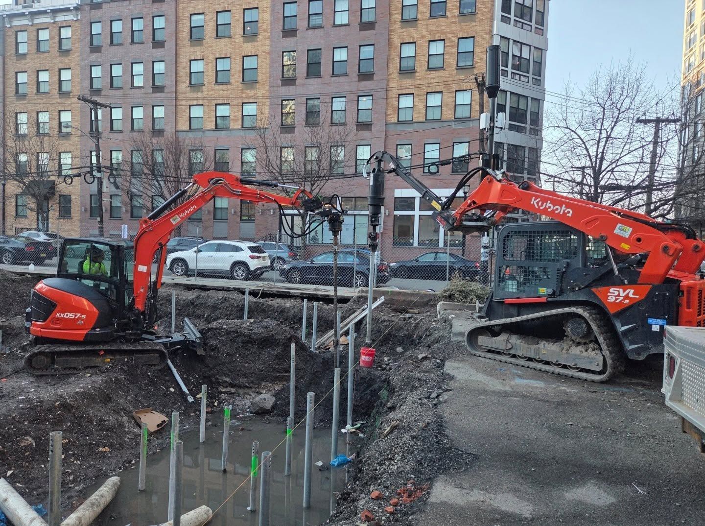 Two compact machines installing piles on a commercial site